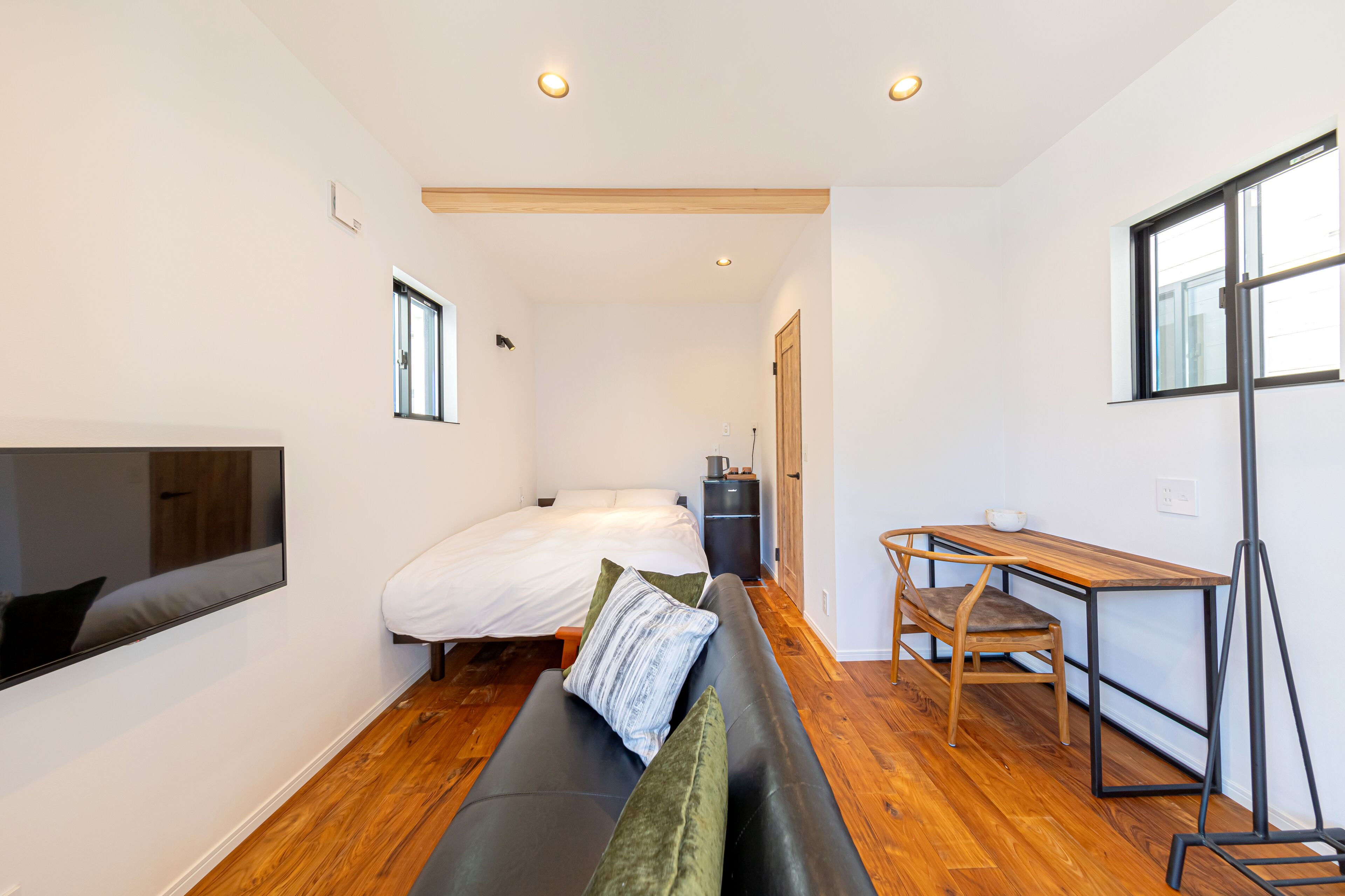 Una habitación compacta con cama, sofá, escritorio y televisor montado en la pared.