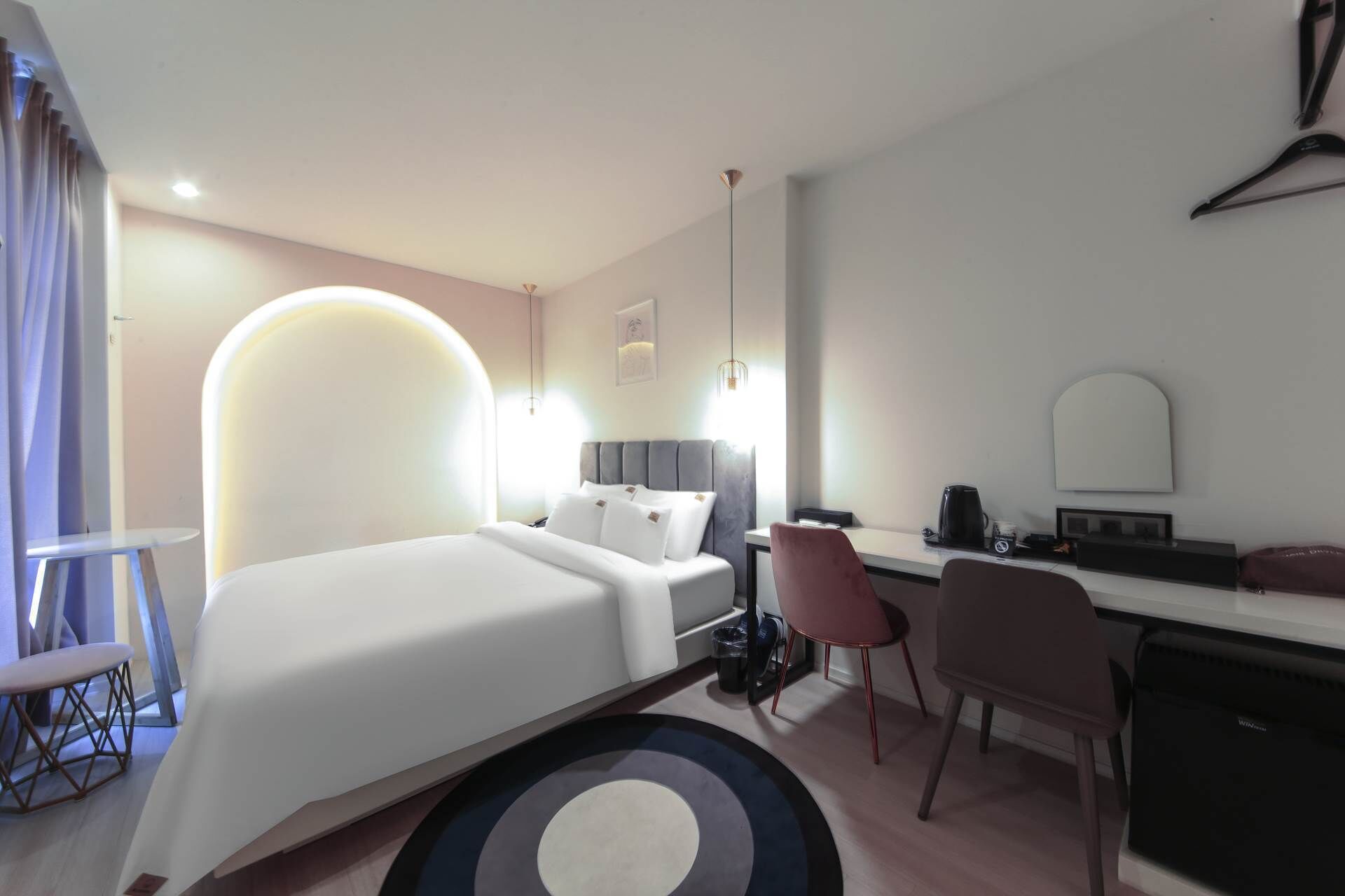 Ein modernes Hotelzimmer mit einem großen Bett, einem Schreibtisch, einem Sessel, einem kleinen Tisch und einer Kaffeemaschine.