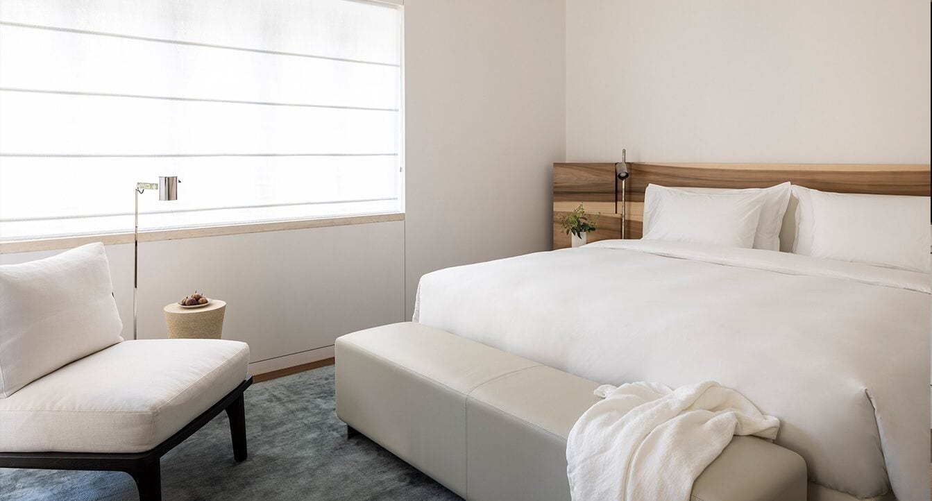 Un dormitorio con una cama, una silla, una mesita de noche y una ventana.