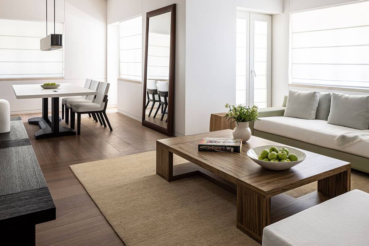 Una sala de estar moderna con comedor, un sofá, una mesa de centro con un cuenco de fruta y un espejo grande.