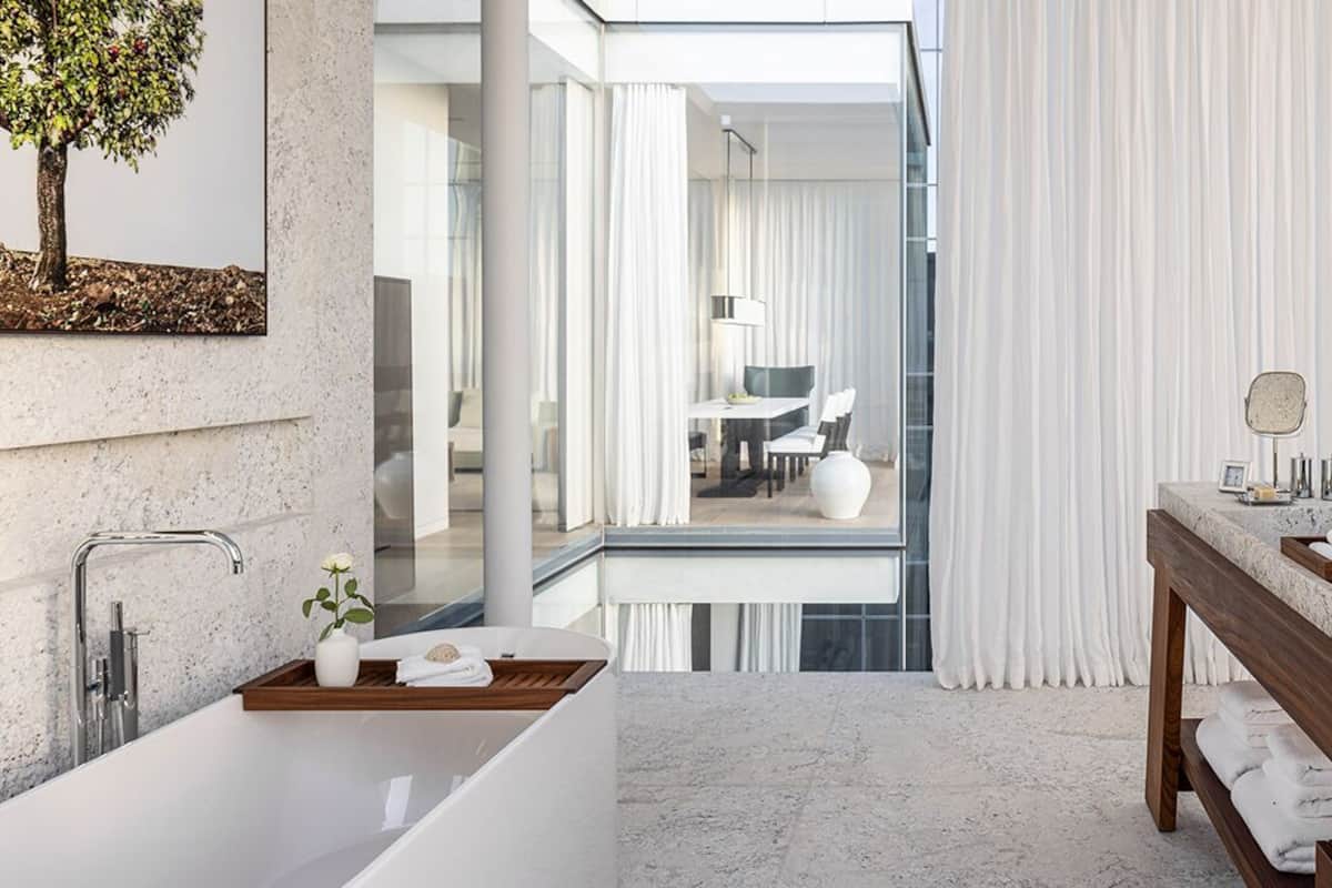 Un baño moderno con una bañera grande, un tocador con espejo y vista a un comedor a través de una puerta de cristal.