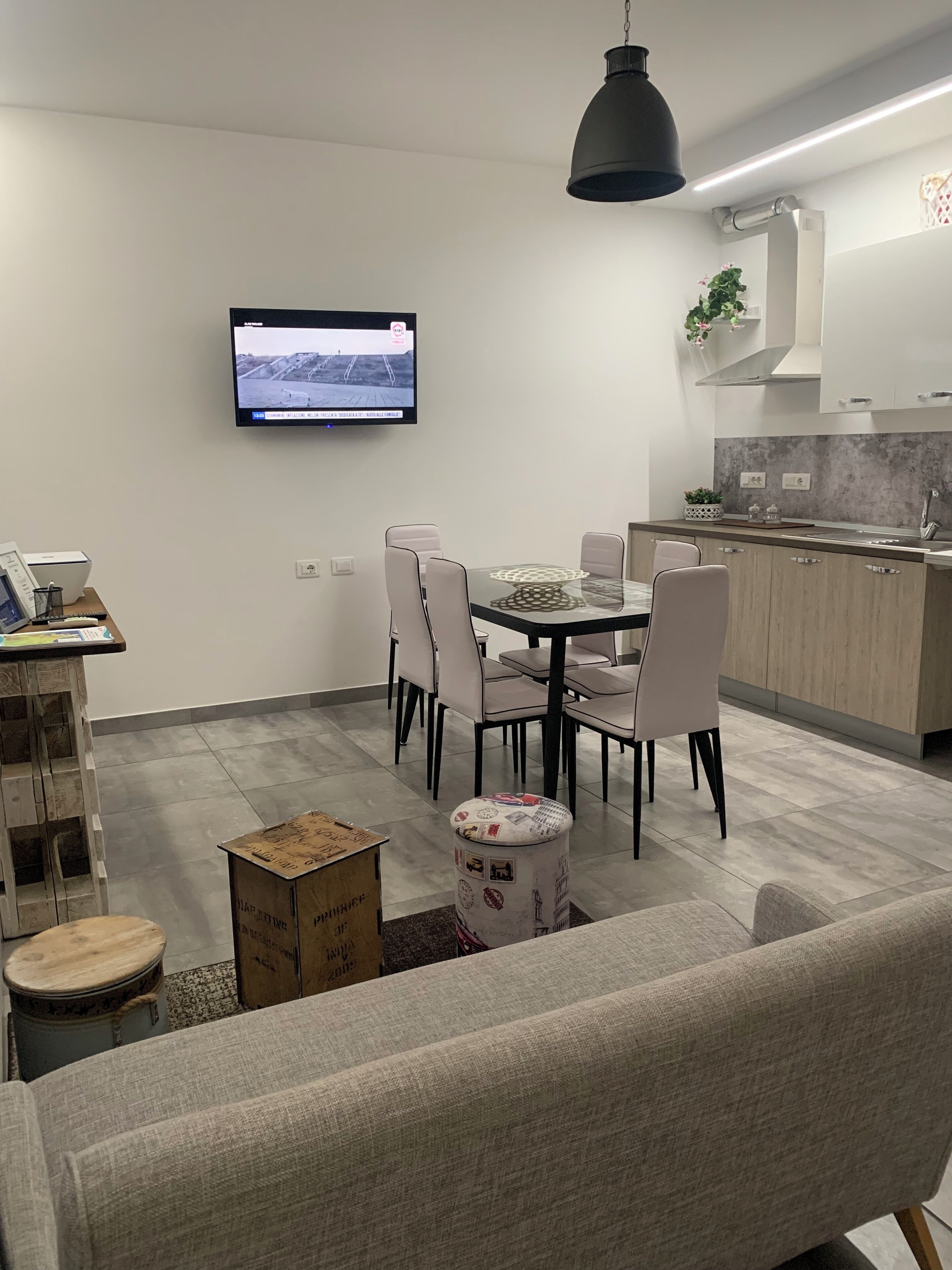 Un salon moderne comprenant un coin repas, une cuisine avec un revêtement mural gris et un téléviseur à écran plat fixé au mur.