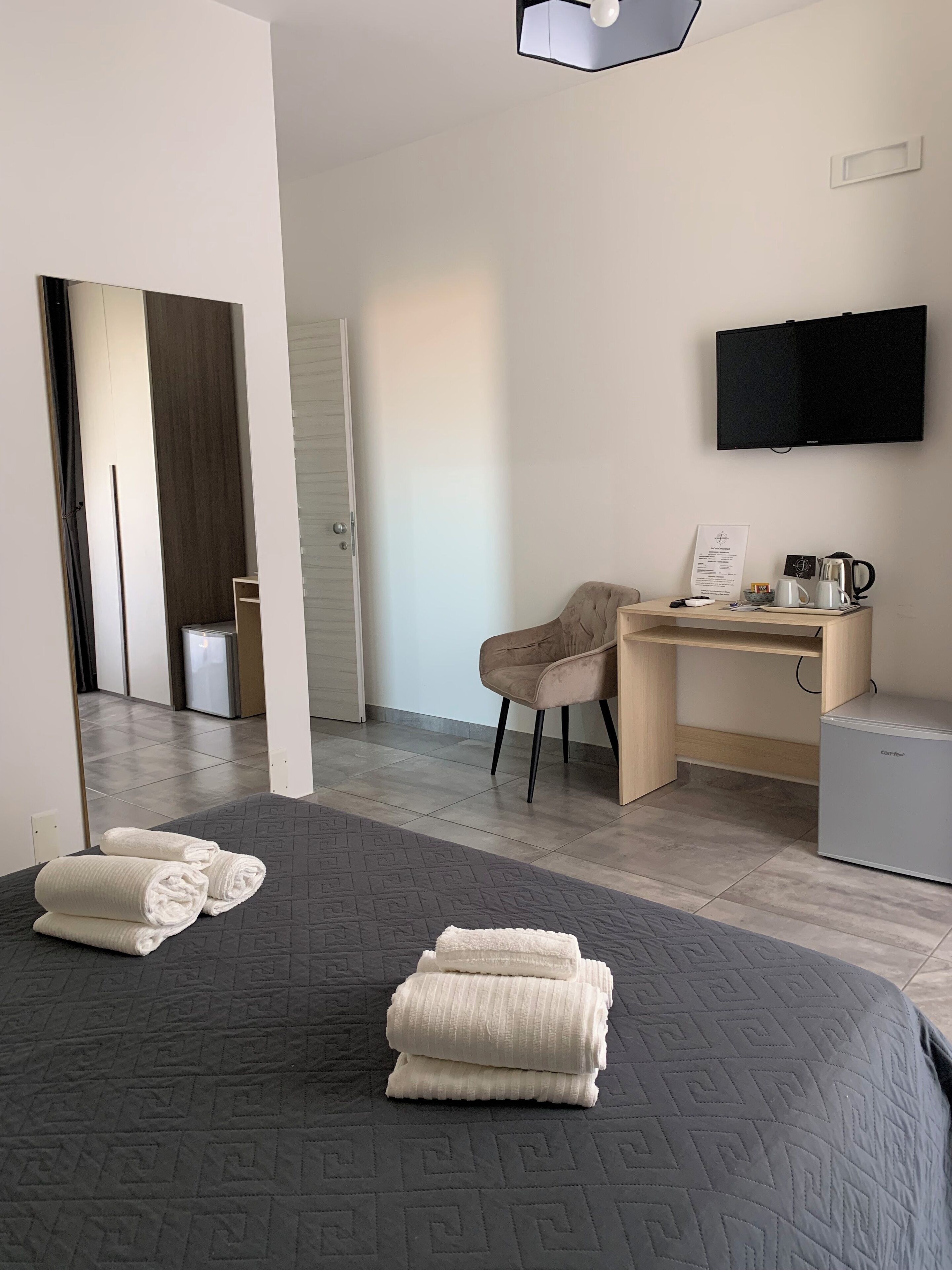 A hotel room with a bed, a desk, a chair, a television, and a small refrigerator.