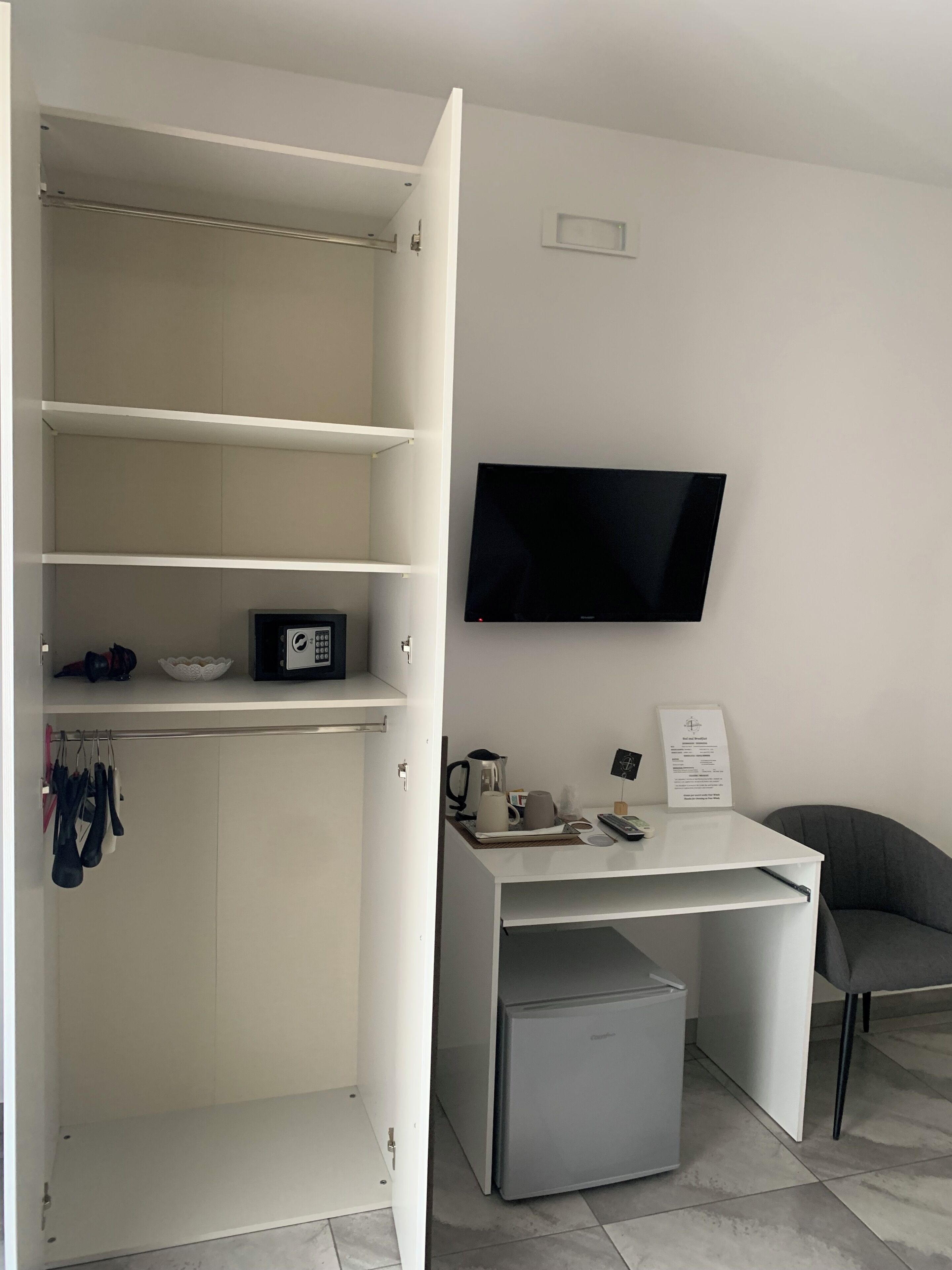 Een moderne, minimalistisch ingerichte kamer met een ingebouwd bureau, een flatscreen-tv en een compacte koelkast.