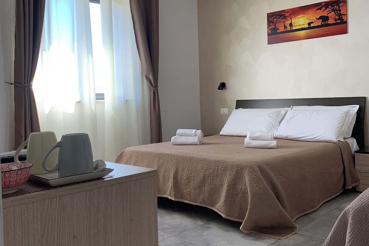 A hotel room with a bed, a desk, a lamp, and a painting on the wall.
