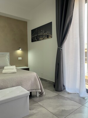 A bedroom with a bed, a nightstand, a wall-mounted light, a painting, and a window with curtains. - Four winds bed and breakfast (Isola di Capo Rizzuto)