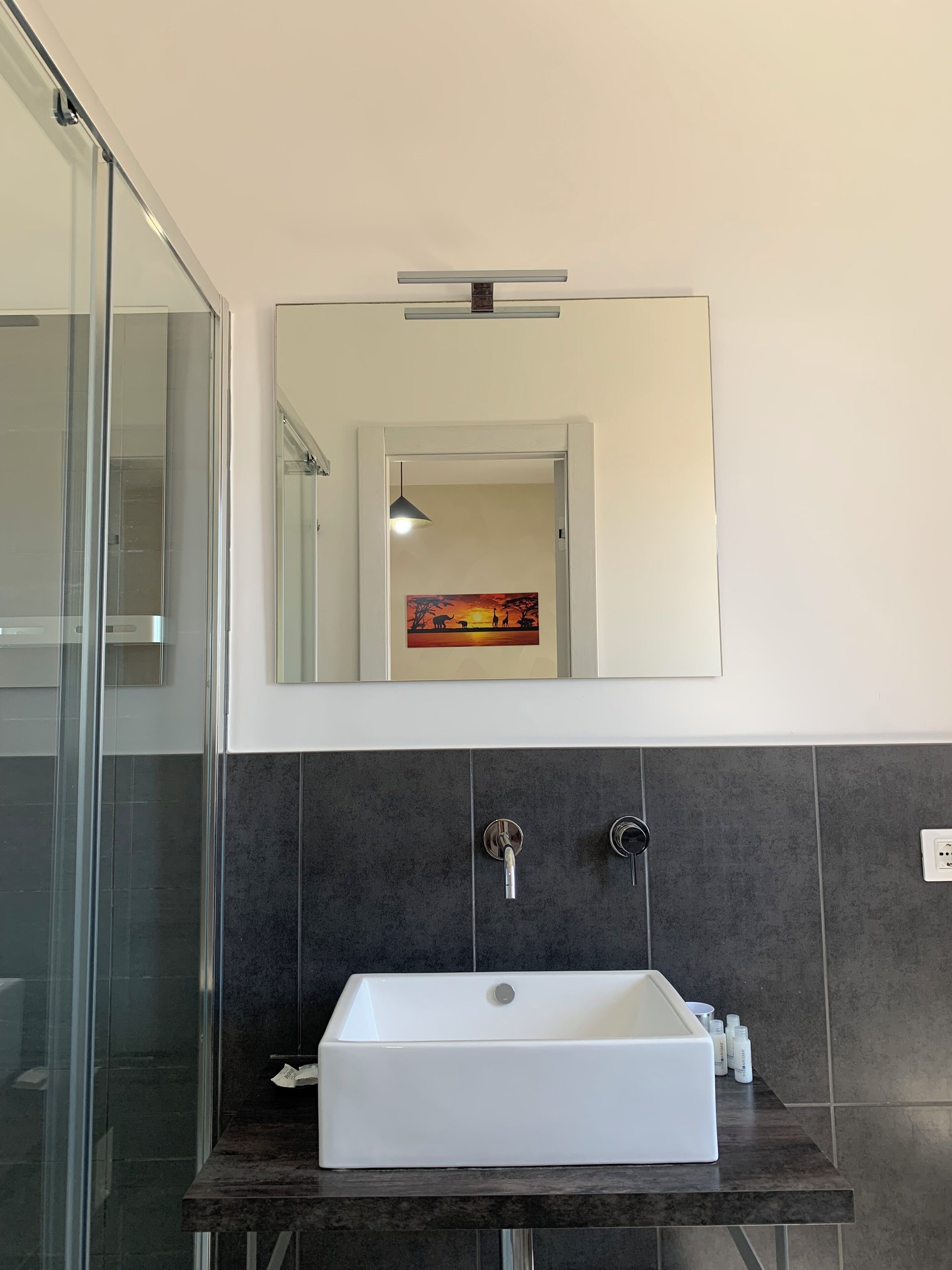 A modern bathroom with a rectangular sink, dark tiled walls, and a large mirror above it.