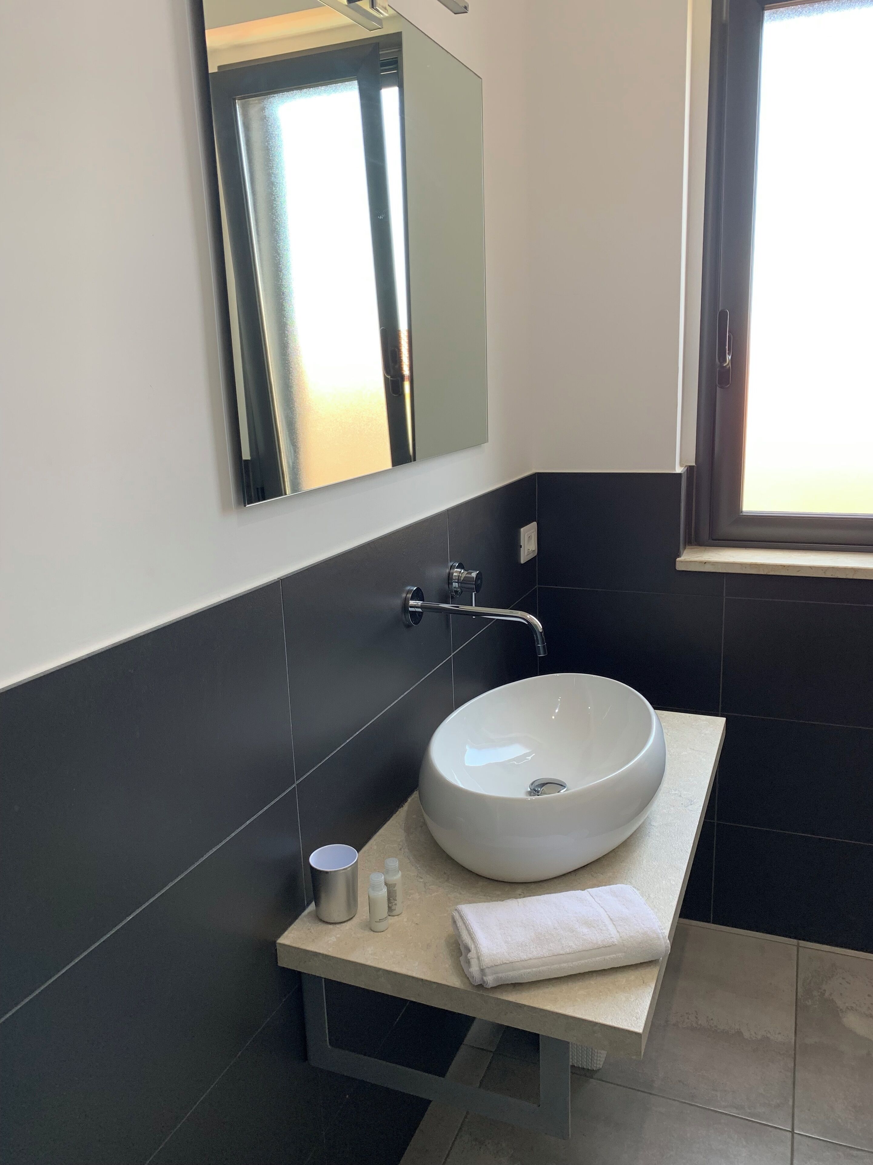 A modern bathroom with a white sink, a mirror, and a window.