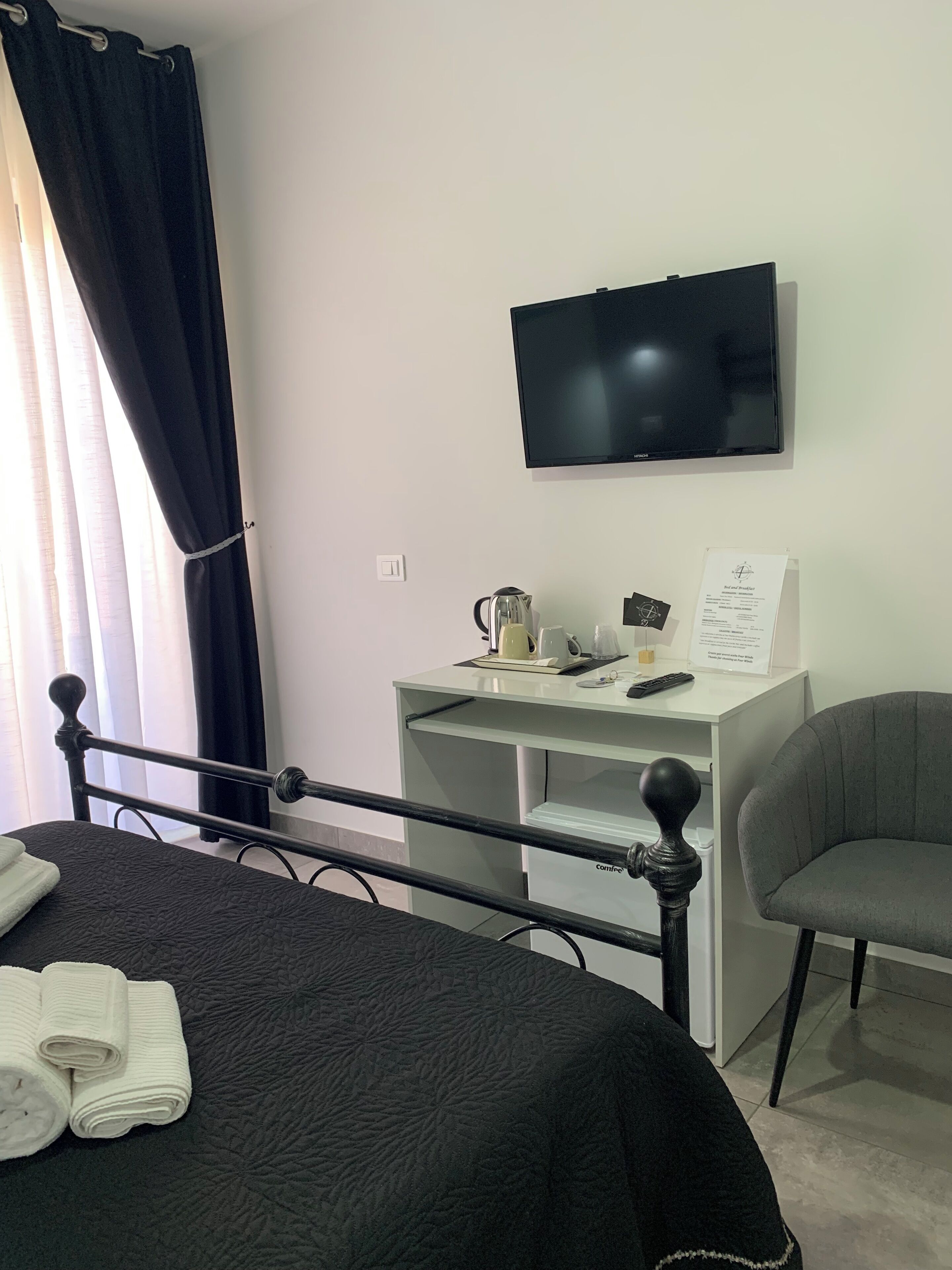 A hotel room with a bed, a desk with a flat-screen TV, a chair, and a coffee station.