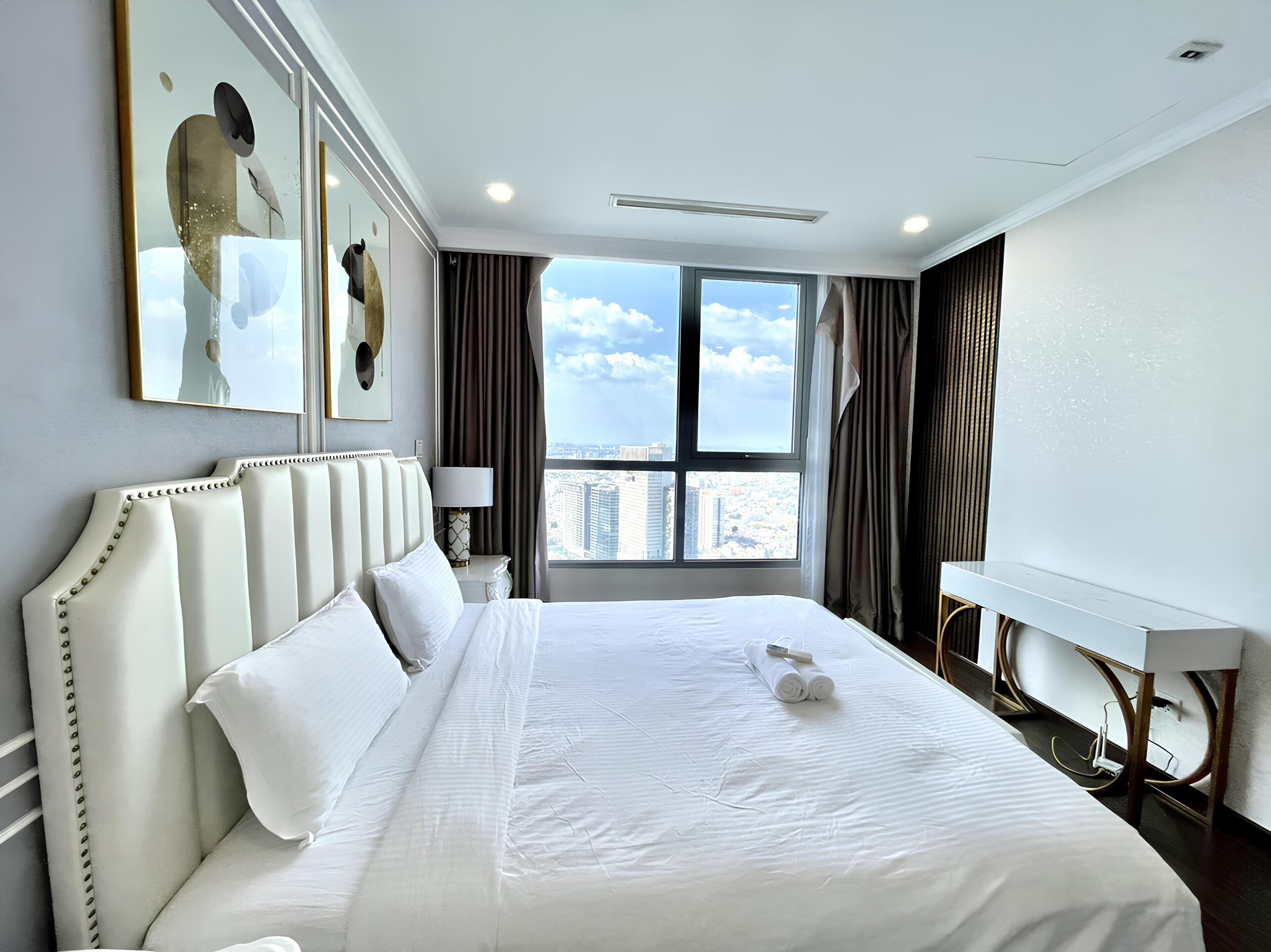 A hotel room with a large bed, a bedside table with a lamp, a view of the city through a large window, and a modern design.