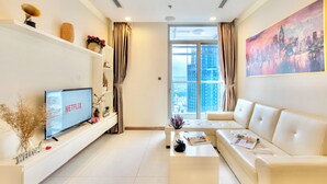 Een moderne woonkamer met een flatscreen televisie, een bank, een salontafel en een groot raam met uitzicht op de stad.