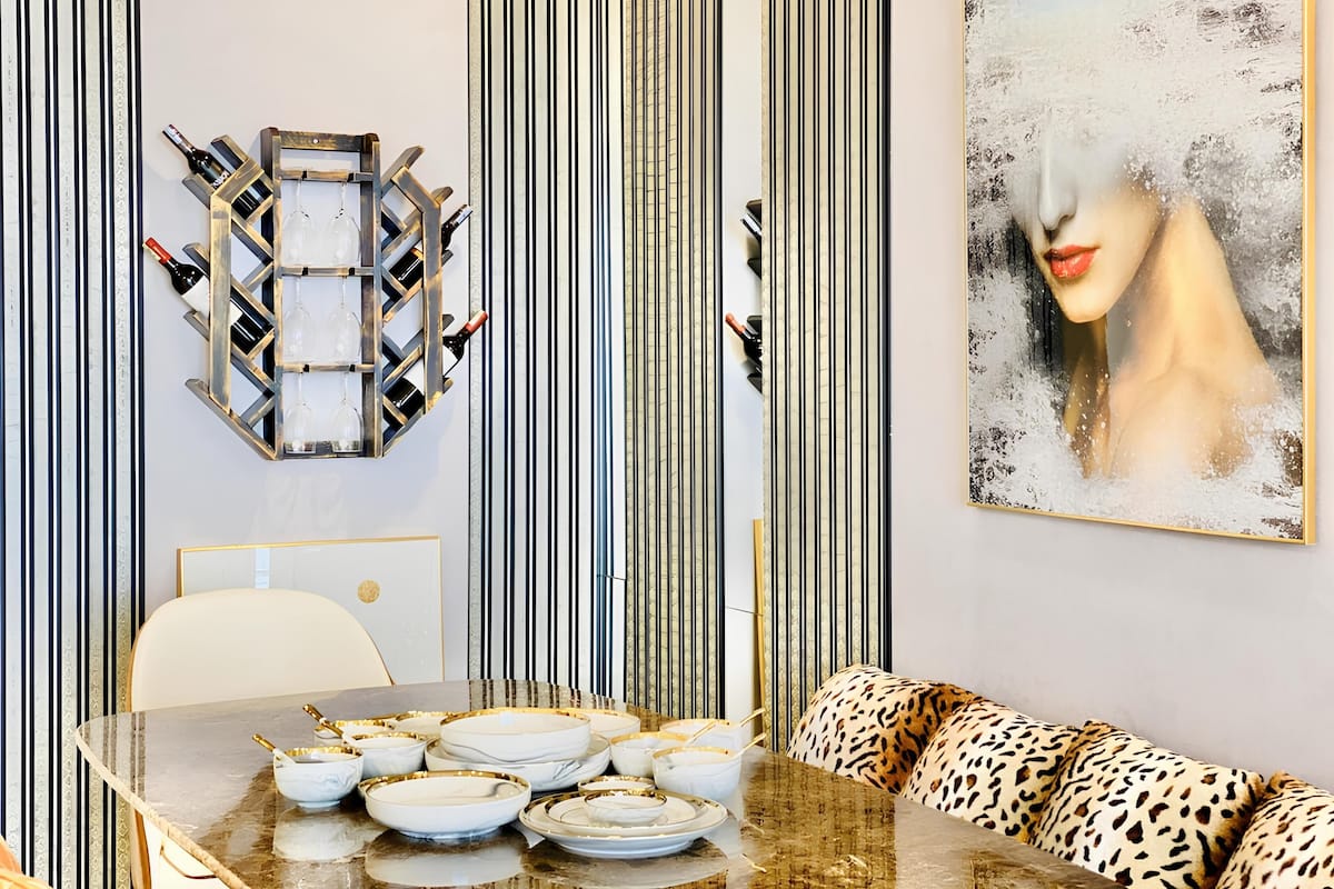 Un coin repas avec une table en marbre dressée pour le repas, un canapé orné de coussins à motifs léopard et un porte-bouteilles fixé au mur.