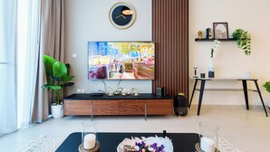 A modern living room with a large flat-screen TV, a wooden entertainment unit, a dining table with candles, and a potted plant. - Marco Polo - Cozy 2BR With Splendid Dubai Frame&Skyline View (Dubai)