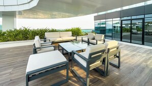 A modern outdoor seating area with a sofa and tables, surrounded by greenery and overlooking a cityscape. - Marco Polo - Cozy 2BR With Splendid Dubai Frame&Skyline View (Dubai)