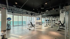 A spacious gym with large windows, various exercise equipment, and a high ceiling. - Marco Polo - Cozy 2BR With Splendid Dubai Frame&Skyline View (Dubai)