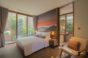 Une chambre d’hôtel avec un grand lit, une table de chevet, une chaise, un tableau et une vue sur la verdure par la fenêtre.