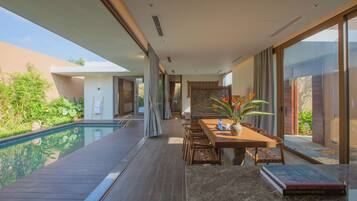 A modern interior with a pool, wooden deck, and a dining area with a book and a plant.