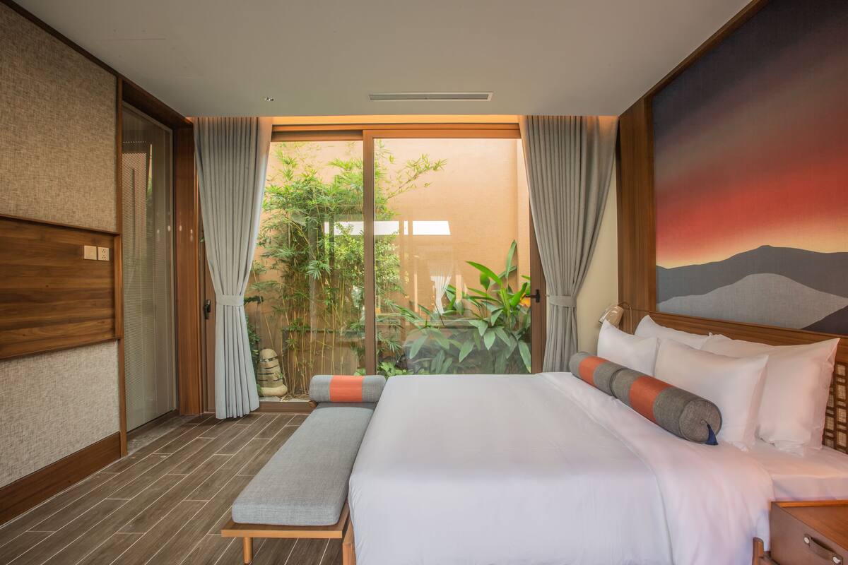 Habitació d'hotel amb un llit gran, una panxa i vista a zones verds per la finestra.