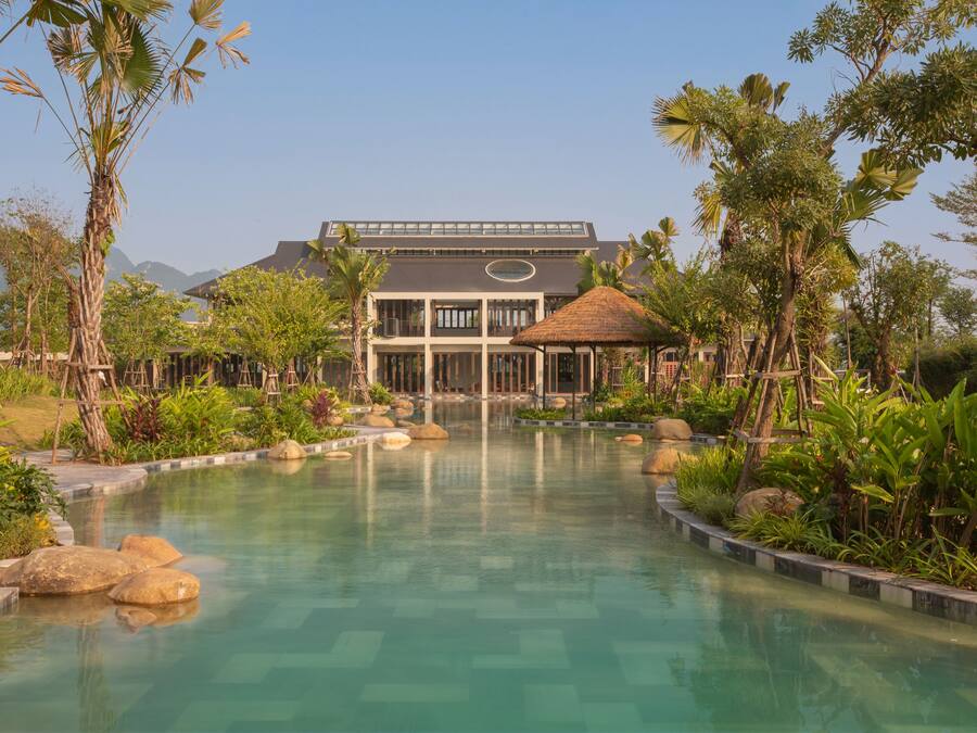 A resort with a swimming pool, a thatched-roof gazebo, and a large building with a modern design.