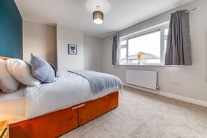 A bedroom with a bed, a window with curtains, a radiator, and a ceiling light. - Modern 3 bed, home from home with free parking (Barnsley)