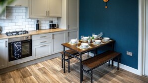 A modern kitchen with white cabinets, a wooden countertop, and a dining table set for four. - Modern 3 bed, home from home with free parking (Barnsley)
