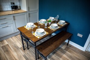 A dining table set with plates, glasses, and a small plant, with a bench and a kitchen area in the background. - Modern 3 bed, home from home with free parking (Barnsley)