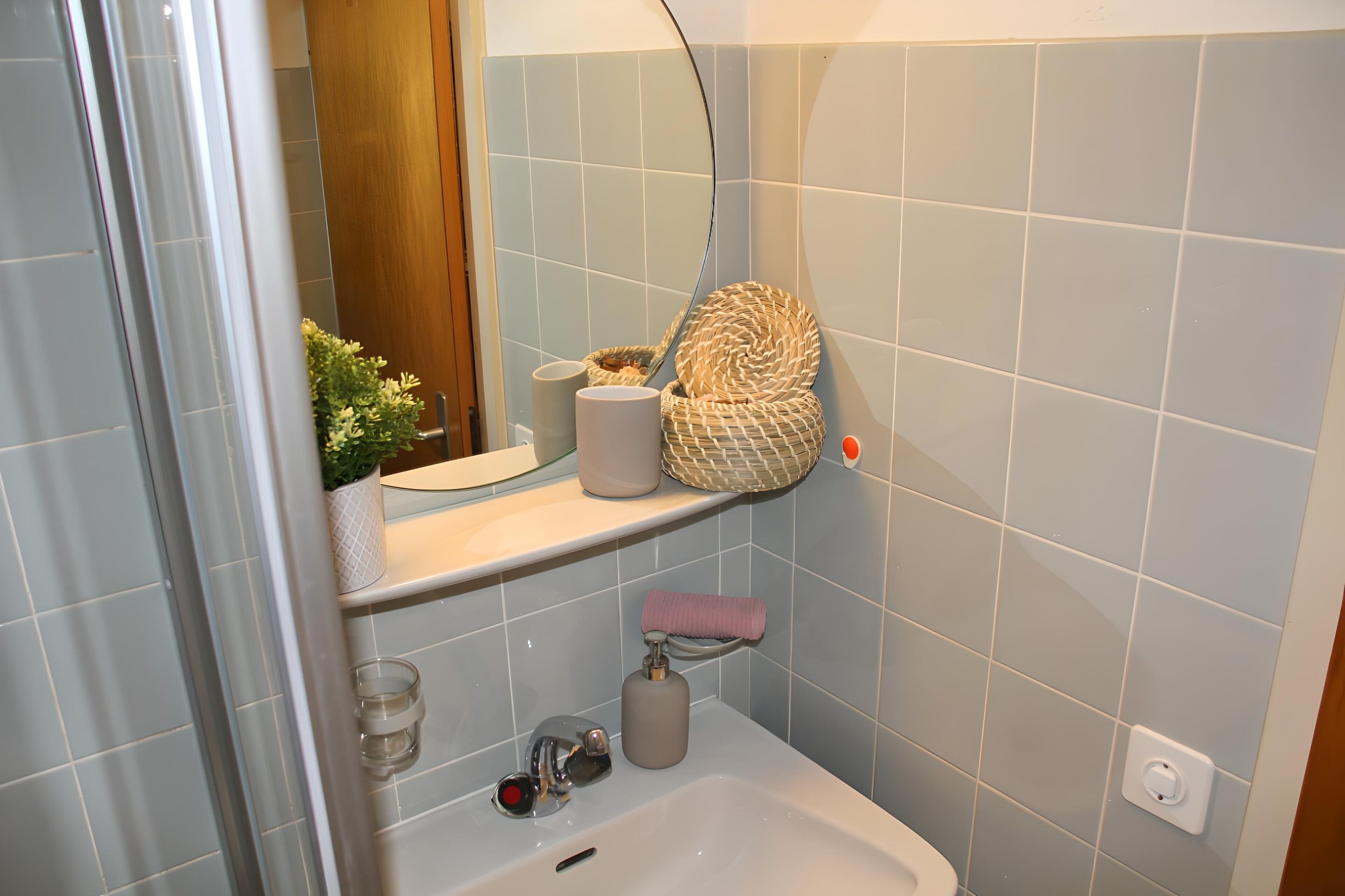 A bathroom with a sink, mirror, and a shelf with toiletries.