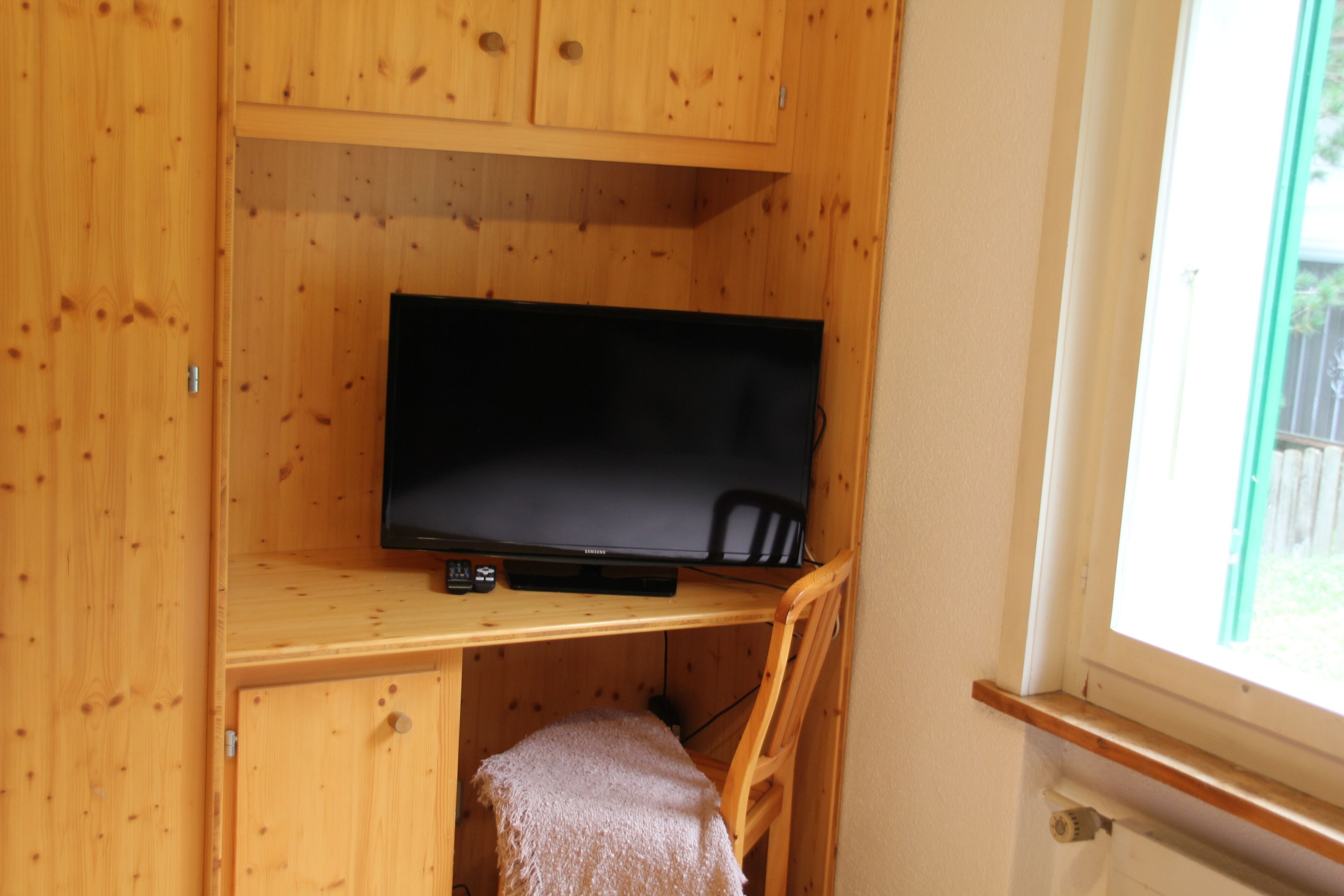 A wooden cabin interior with a television on a shelf, a chair, and a window.