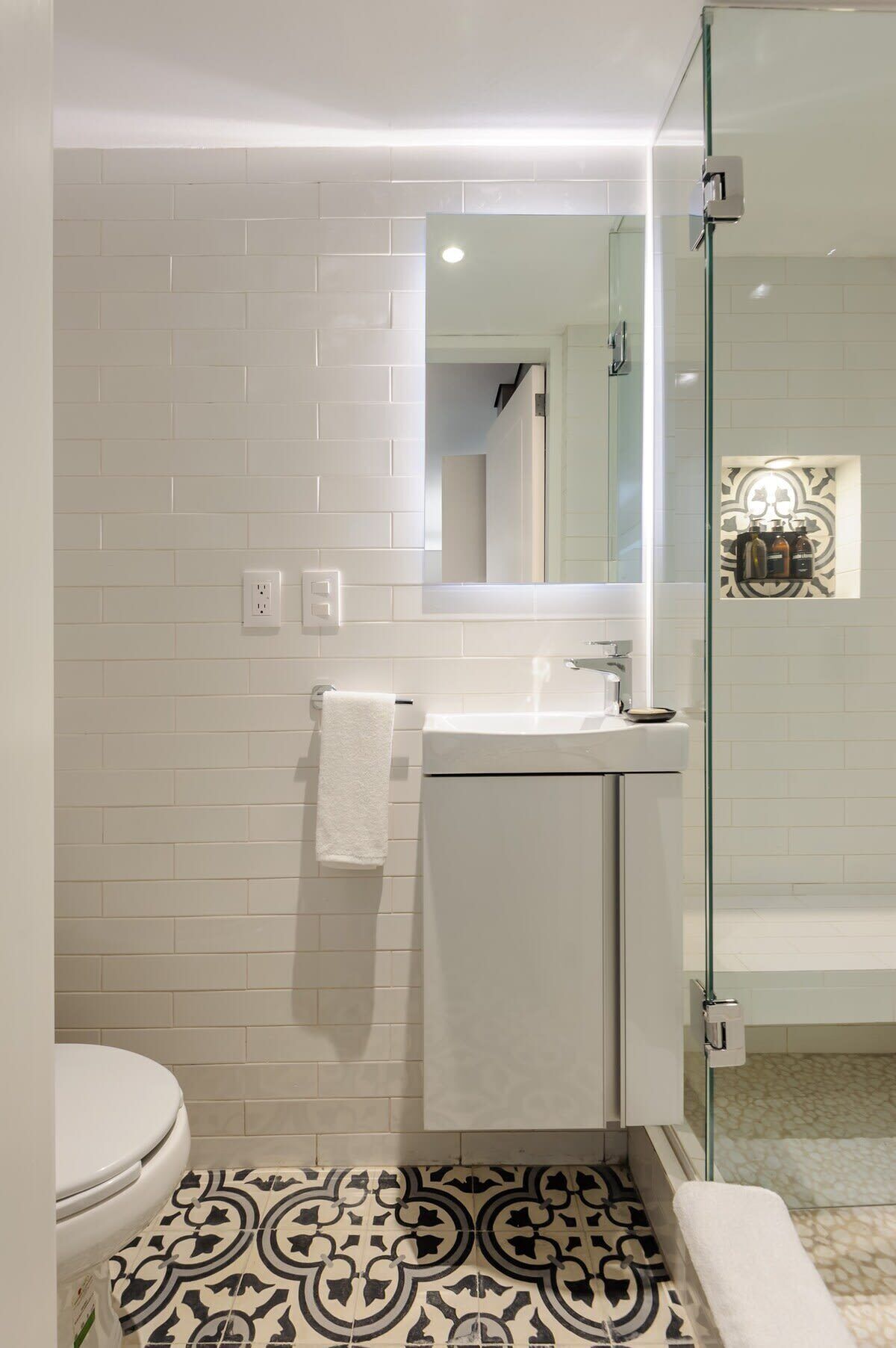 Een moderne badkamer met een witte betegelde wand, een glazen douchecabine, een wit wastafelmeubel en een vloer met een patroon.