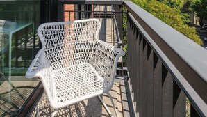 En balkong med en vit flätstol, träribbor och utsikt över stadsbilden.