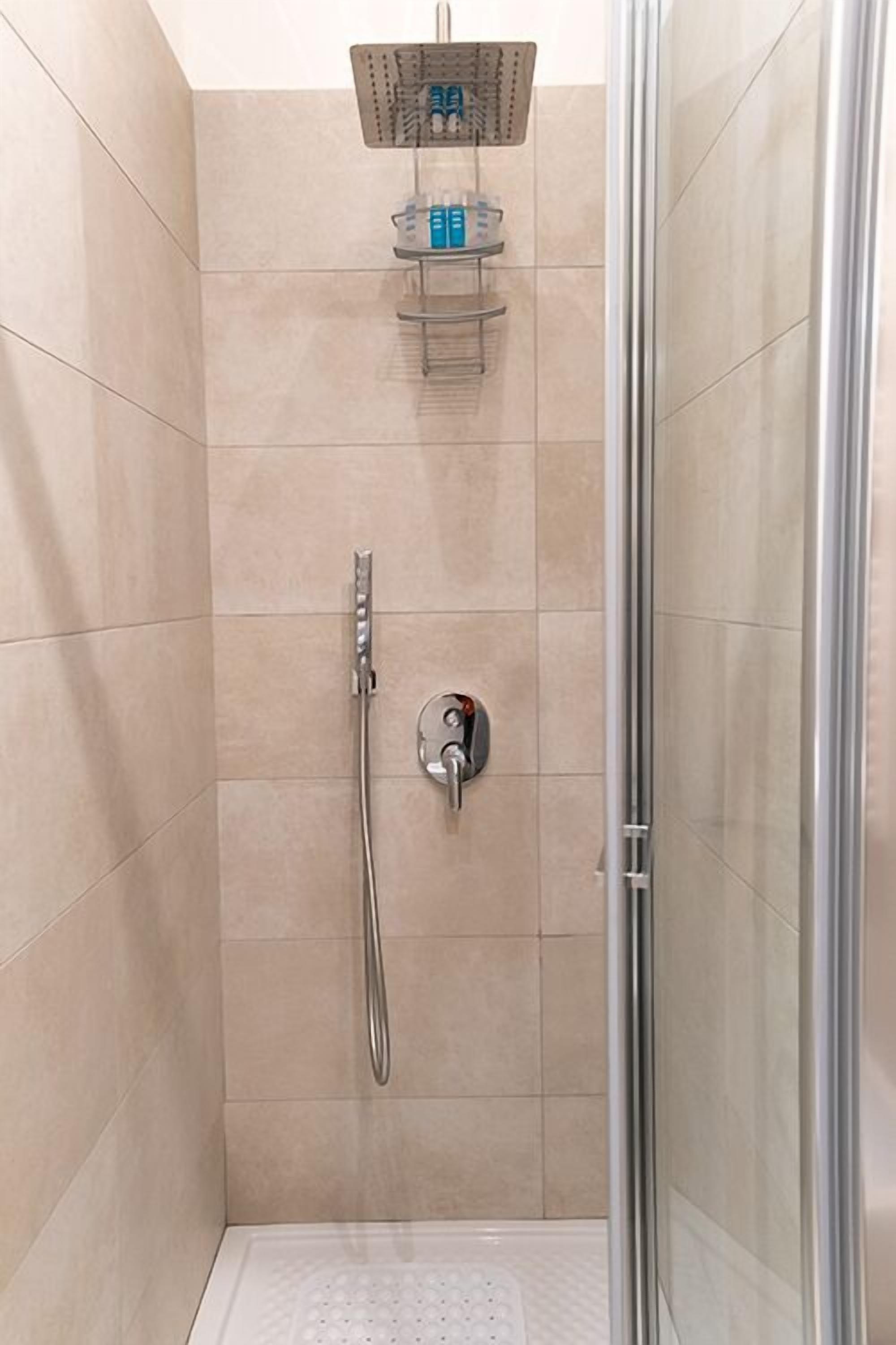A shower area with a handheld showerhead and a wall-mounted control panel.