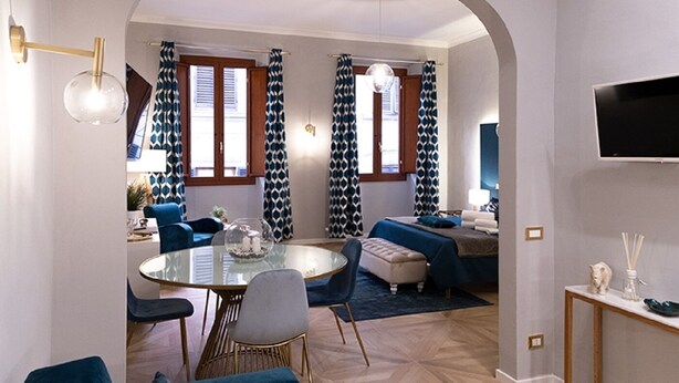 Una sala de estar moderna con una mesa de comedor de cristal, sofás azules y un televisor montado en la pared.
