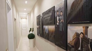 Un pasillo con varias fotografías enmarcadas en la pared, una planta en maceta y una puerta al final.