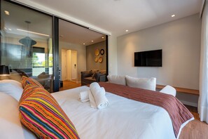 Una habitación de hotel moderna con una cama grande, un sofá, un televisor y un ventanal corredera que da a un balcón.