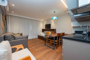 A modern hotel room with a sofa, a dining table with chairs, a bed, a TV, a kitchen area with a sink, and a ceiling-mounted air conditioning unit. - Wanderlust Experience Hotel, BW Signature (Campos do Jordão)