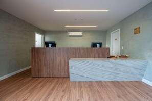 Zona de recepción de un hotel con un mostrador de madera, encimera de mármol y una puerta con un cartel.