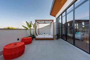 A modern balcony with a wooden canopy bed, red woven ottomans, and large glass windows offering a view of the city. - Wanderlust Experience Hotel, BW Signature (Campos do Jordão)