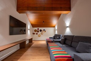 A modern living room with a wooden ceiling, a gray sofa, a colorful striped rug, and a wall-mounted TV. - Wanderlust Experience Hotel, BW Signature (Campos do Jordão)