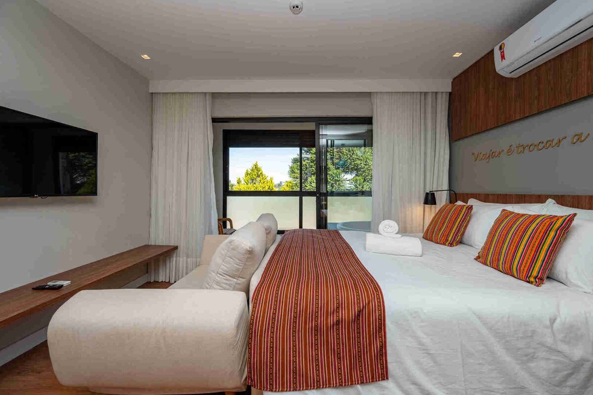 Una habitación de hotel moderna con una cama grande, un sofá, un televisor y un balcón con vistas a árboles.