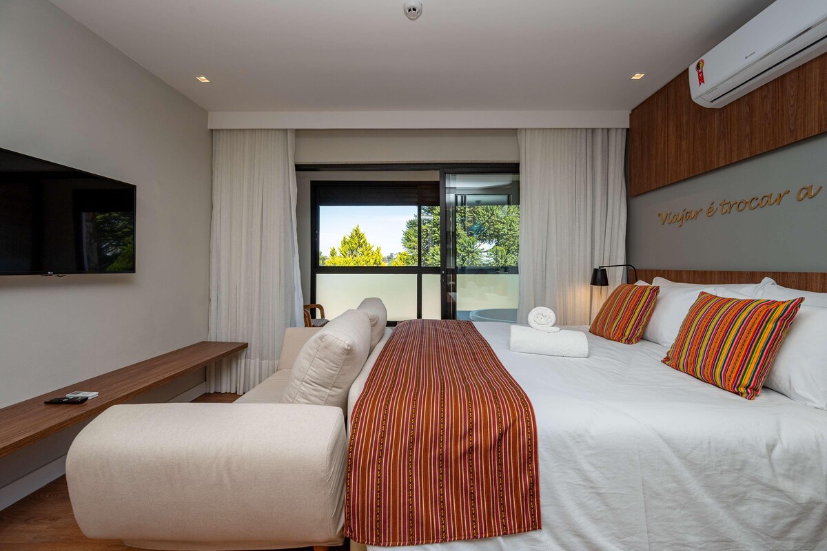 Una habitación de hotel moderna con una cama, un sofá, un televisor y un ventanal grande.