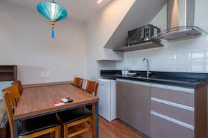 Cocina compacta con microondas, lavamanos y un refrigerador pequeño. Hay una mesa de comedor con sillas y una lámpara en el techo.