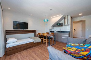 Una habitación moderna con una cama, una mesa de comedor con sillas, una kitchenette y un sofá.