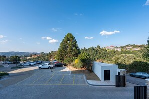 A parking area with multiple cars, a small white building, and a large tree. - Wanderlust Experience Hotel, BW Signature (Campos do Jordão)