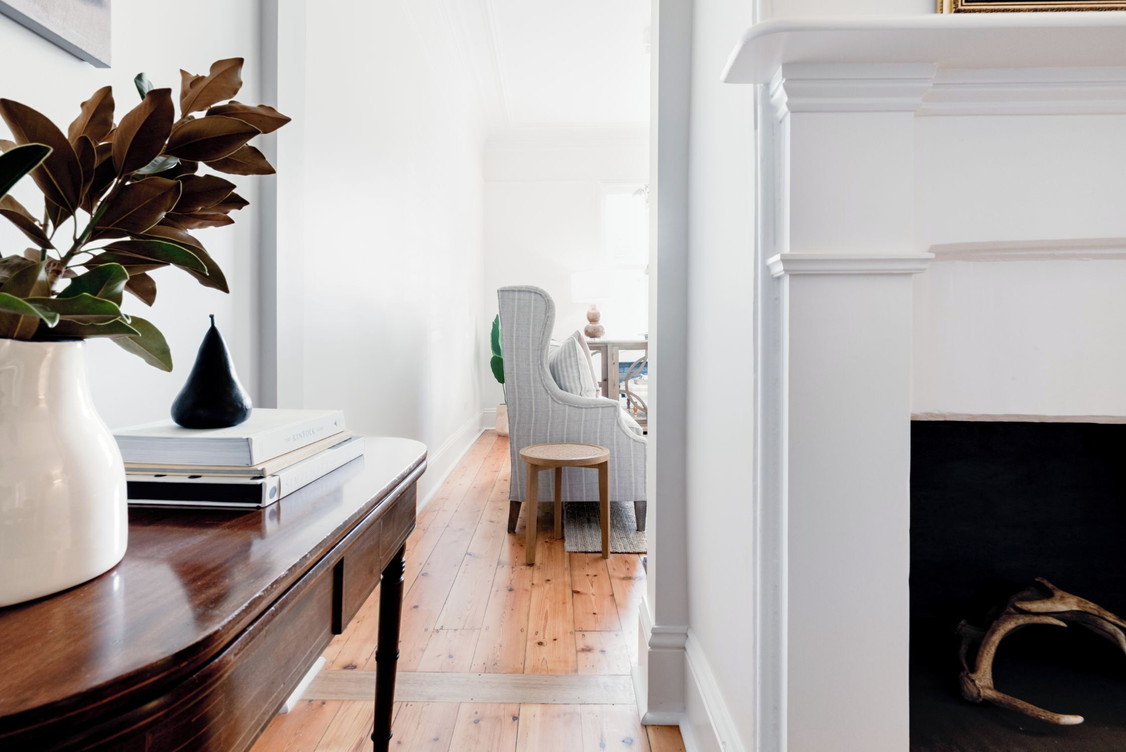 A hallway with a wooden floor, a white fireplace, and a chair in the background.