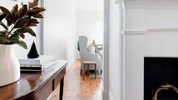 A hallway with a wooden floor, a white fireplace, and a chair in the background.