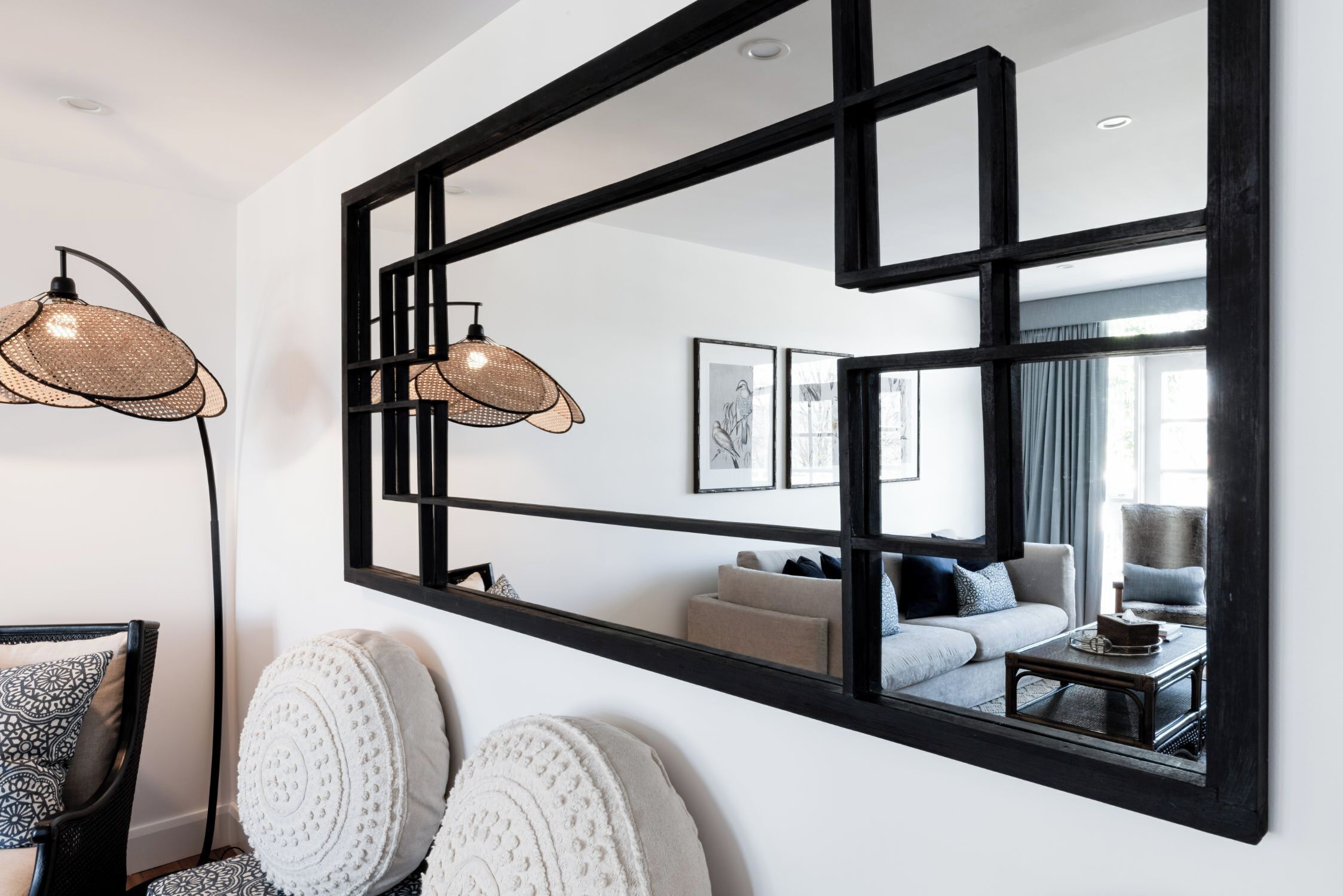 A modern living room with a large mirror, two wicker lamps, and a sofa with cushions.