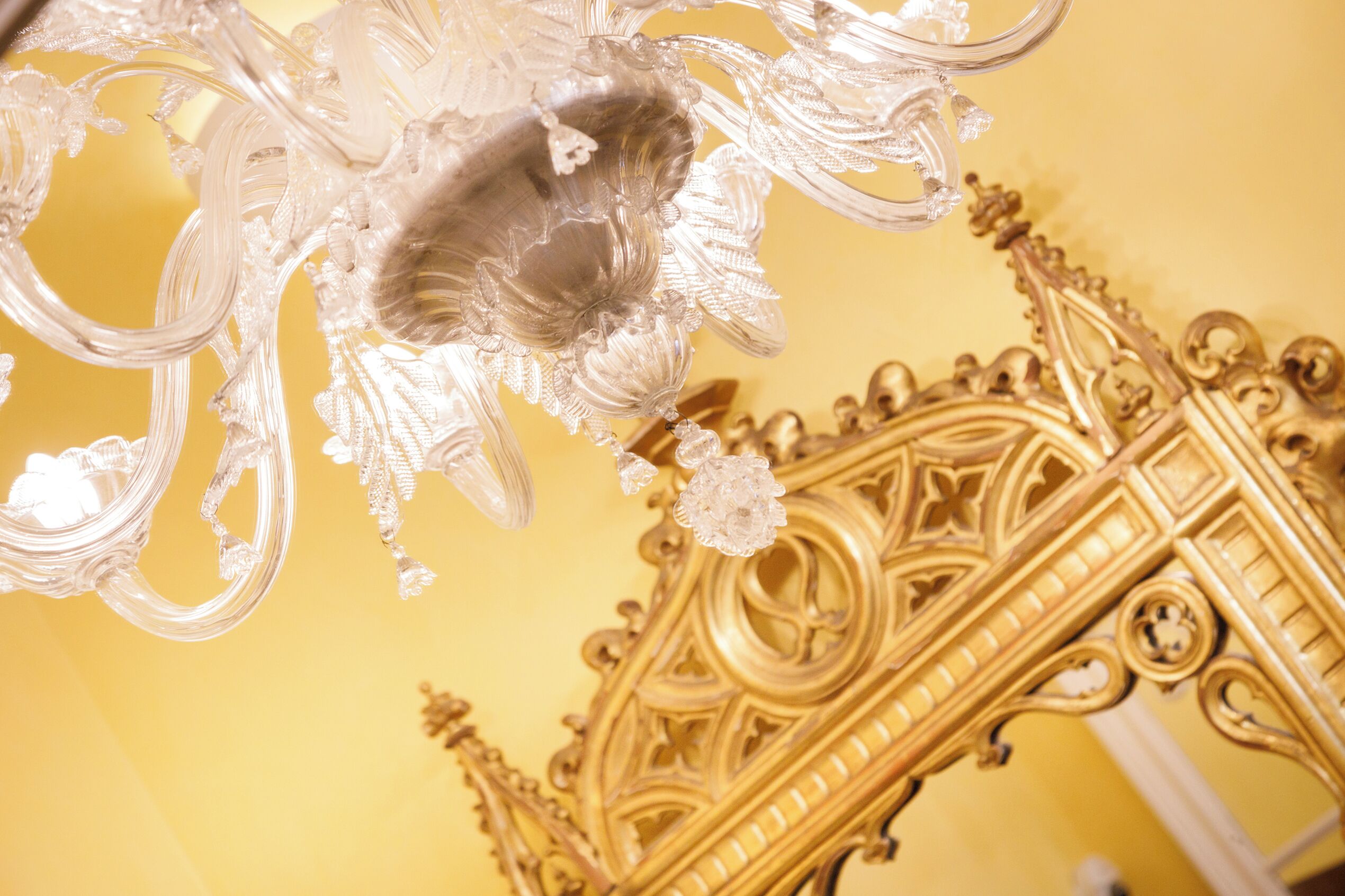 A chandelier with intricate glass details and a golden ornate bed frame.