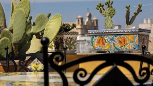 A cactus plant, a decorative ceramic pot, and a metal fence in a courtyard with a building in the background. - Saint George's House Apartments & SPA (Pachino)