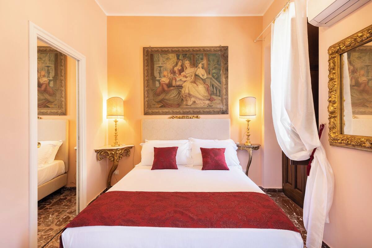 A hotel room with a large bed, two bedside lamps, a painting on the wall, and a mirror with a gold frame.