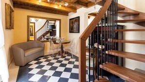 A modern interior with a wooden staircase, a checkered floor, a dining area with a round table and chairs, and a sofa. - Saint George's House Apartments & SPA (Pachino)